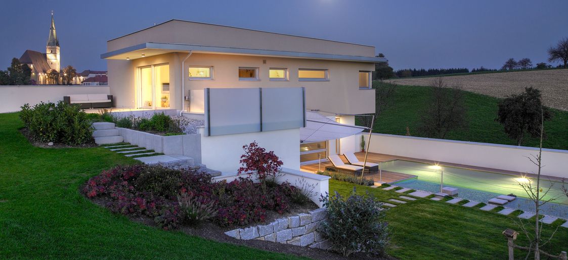 Haus mit großem Garten und Außenbeleuchtung am Abend